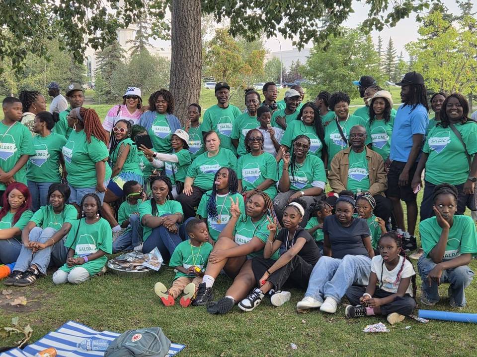Dozens of SALDAC members and their children in matching green SALDAC T-shirts, gathered under the trees at the 2026 Picnic in the Park