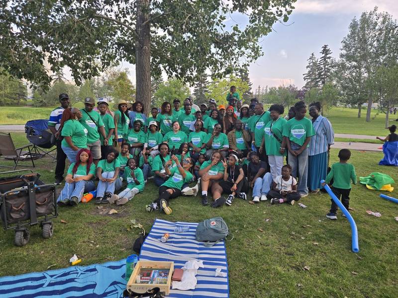 A wide group photo of SALDAC families in green T-shirts in a Calgary park